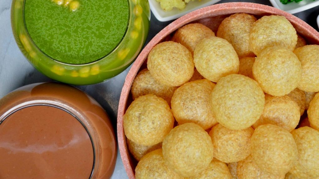 초록색 처트니, 갈색 소스, 노란색 감자 작은 접시 옆에 동그랗고 바삭한 퓨리 한 바구니.