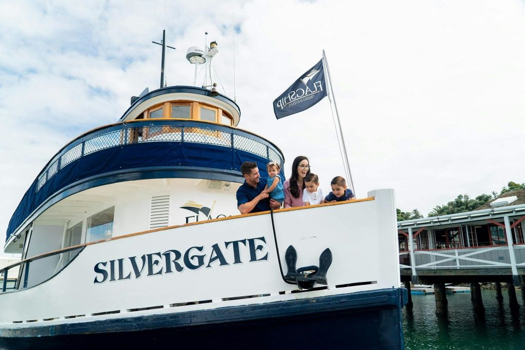 5인 가족이 '실버게이트' 라는 이름의 보트 갑판에 서서 미소를 짓고 물 너머를 내다보고 있습니다.