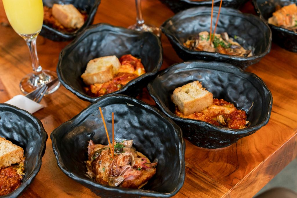 빵 조각과 꼬치로 장식된 음식이 담긴 검은 그릇이 나무 테이블 위에 놓여 있습니다.