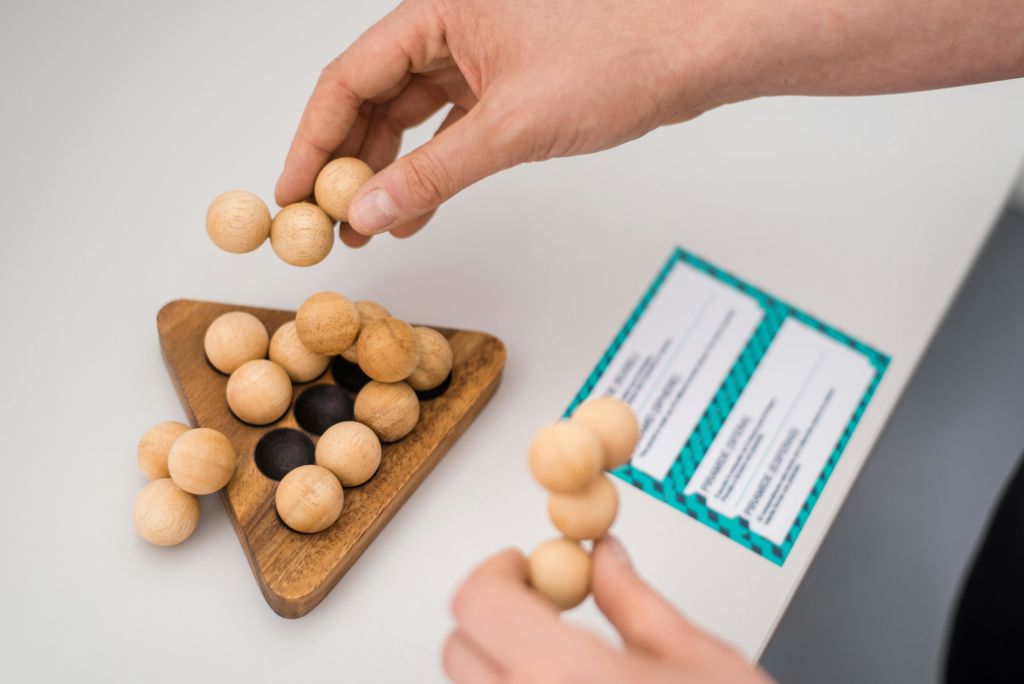 카드를 배경으로 삼각형 베이스에 나무 구슬 퍼즐을 조립하는 손.