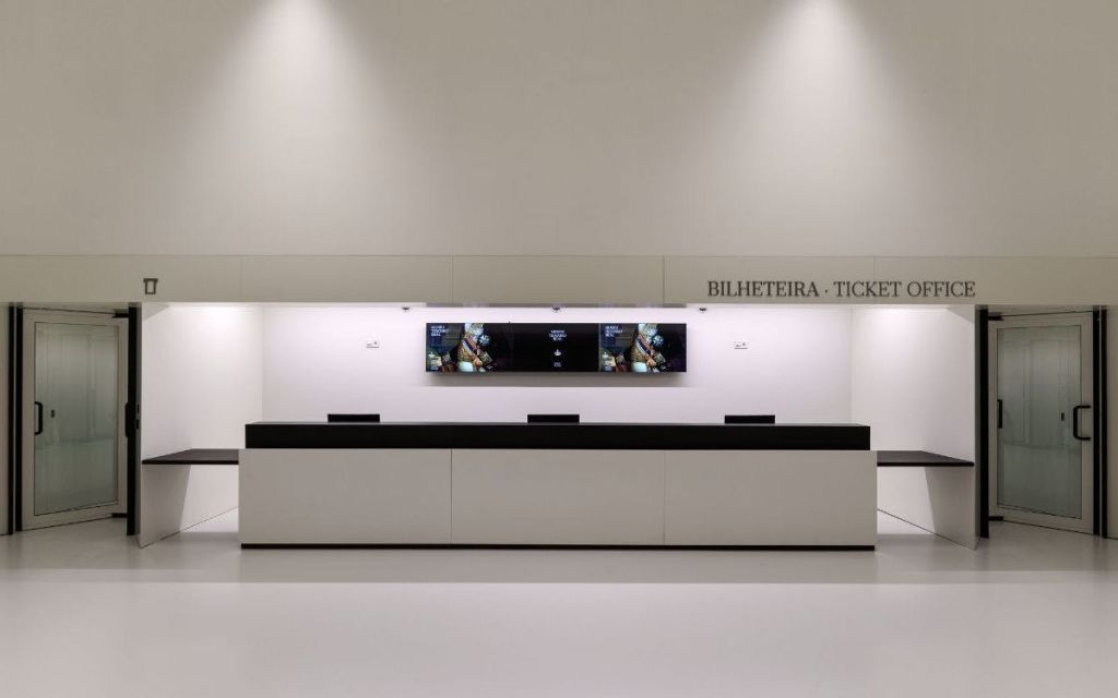 세 개의 화면에 정보가 표시되고 그 위에 "Bilheteira · Ticket" 이라는 단어가 표시된 티켓 카운터.