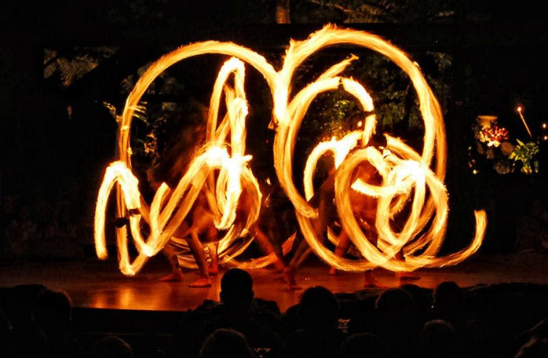 공연자들은 어두운 환경에서 불꽃으로 복잡한 패턴을 만들고, 관객의 실루엣은 전경에서 볼 수 있습니다.