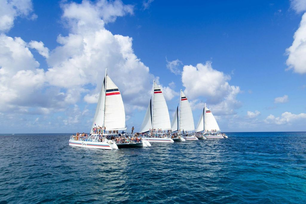 바다에 줄무늬 돛을 단 흰 쌍동선 네 대는 흩어진 구름과 함께 푸른 하늘 아래 사람들로 가득합니다.