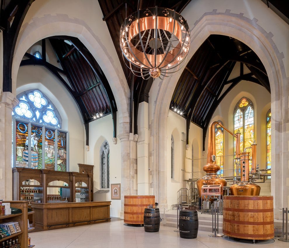 개조된 교회의 내부에는 커다란 아치형 창문, 샹들리에, 증류 장비, 나무 통이 있습니다.
