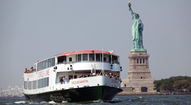 "서클 라인 맨해튼" 이라고 쓰여진 보트가 맑은 날 자유의 여신상을 지나갑니다.