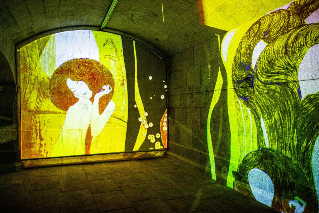 머리카락이 흐르는 형상이 특징인 추상적이고 꽃무늬 예술의 다채로운 투영으로 조명된 아치형 석실.
