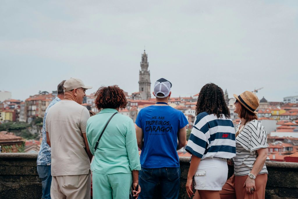 역사적인 건물과 높은 타워가 있는 도시 풍경을 내려다보며 4명이 카메라를 등지고 서 있습니다.