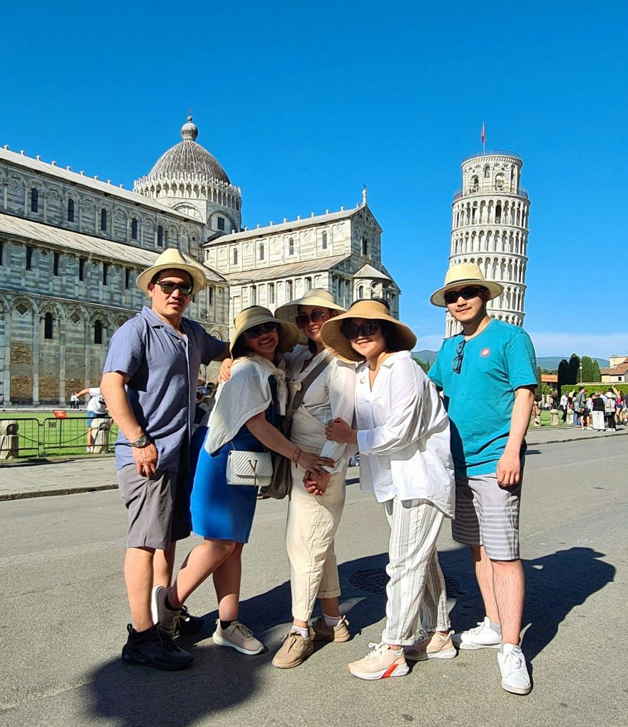 화창한 날 피사의 사탑과 피사 대성당 앞에서 포즈를 취하고 있는 5명의 일행이 여름 복장을 하고 있습니다.