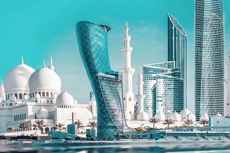 기울어진 유리 마천루, 하얀 돔형 건물, 맑은 하늘 아래 높이 솟은 대저택이 있는 현대적인 도시 풍경입니다.