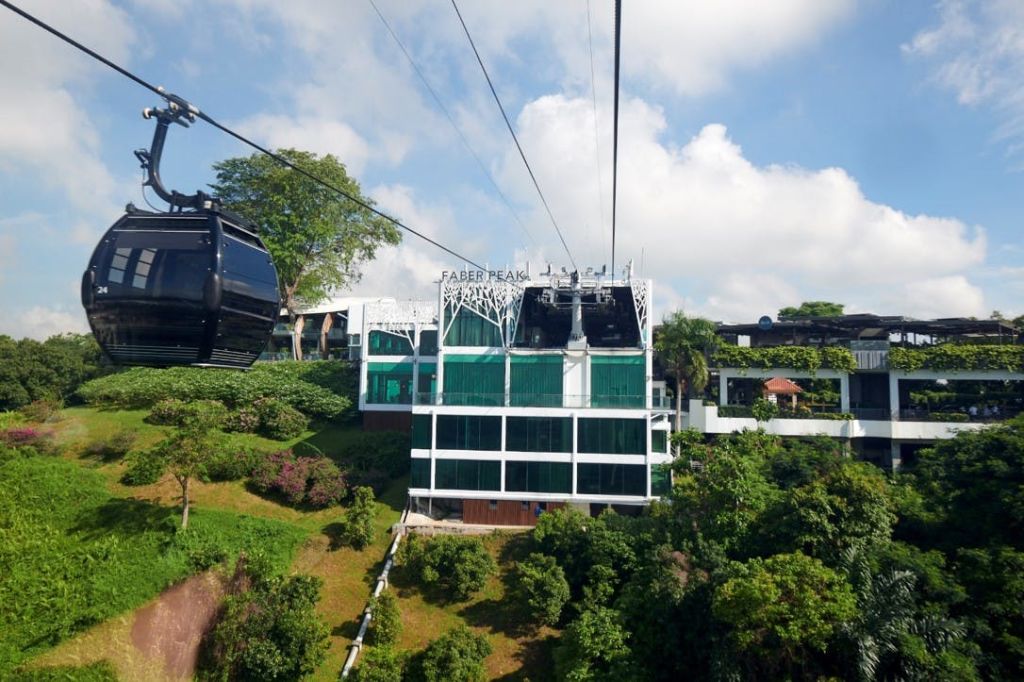부분적으로 흐린 하늘 아래 무성한 녹음으로 둘러싸인 페이버 피크 (Faber Peak) 역으로 접근하는 공중 케이블카.