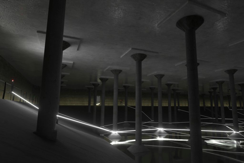 콘크리트 기둥, 반사되는 물, 조명 선으로 어두운 지하 구조물이 현대적인 미를 연출합니다.