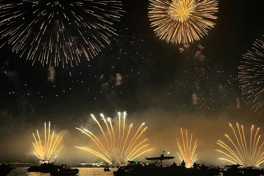 물 위의 밤하늘을 비추는 불꽃놀이와 전경의 보트.