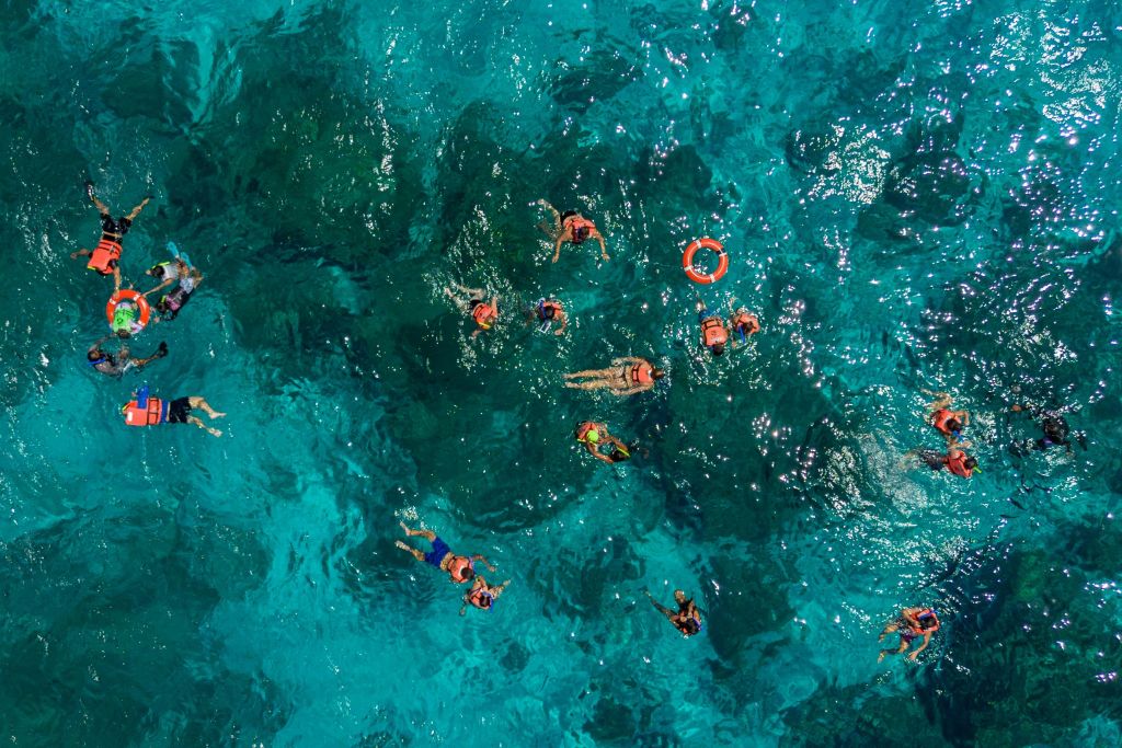 청록색의 맑은 물에서 수영하는 사람들 중 일부는 구명조끼를 입고 근처에 붉은 수레를 타고 있습니다.