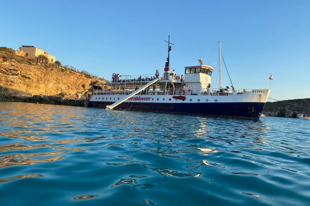 '혼블로어 (Hornblower)' 라는 이름의 보트가 맑고 푸른 하늘 아래 바위 해안 근처에 정박했고, 사람들이 탑승했으며, 전경에는 잔잔한 푸른 물이 흐르고 있었습니다.