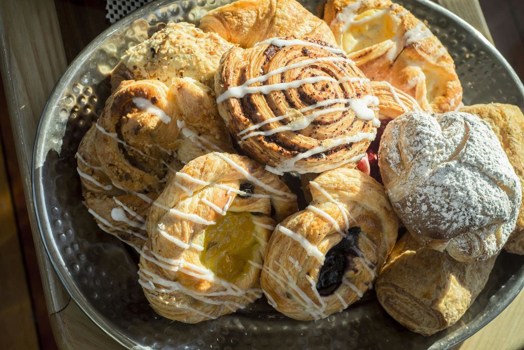 계피 롤, 과일 데니쉬, 크루아상을 포함한 다양한 페이스트리가 아이싱 드리즐이 있는 플래터에 쌓여 있습니다.