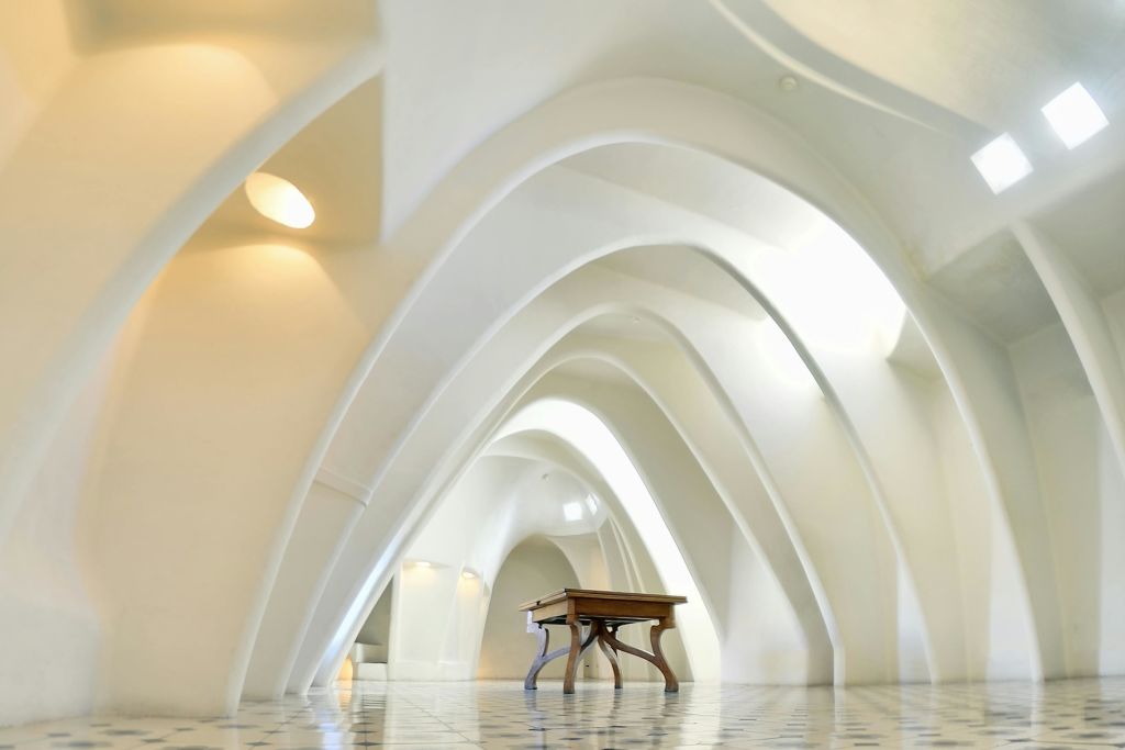 나무 테이블이 일련의 곡선형 및 흐르는 흰색 아치 아래 무늬가 있는 타일에 서 있어 밝고 쾌적한 공간을 연출합니다.