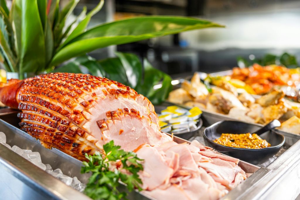 파슬리로 장식된 조각된 햄은 다른 요리를 배경으로 뷔페에 전시되어 있습니다.