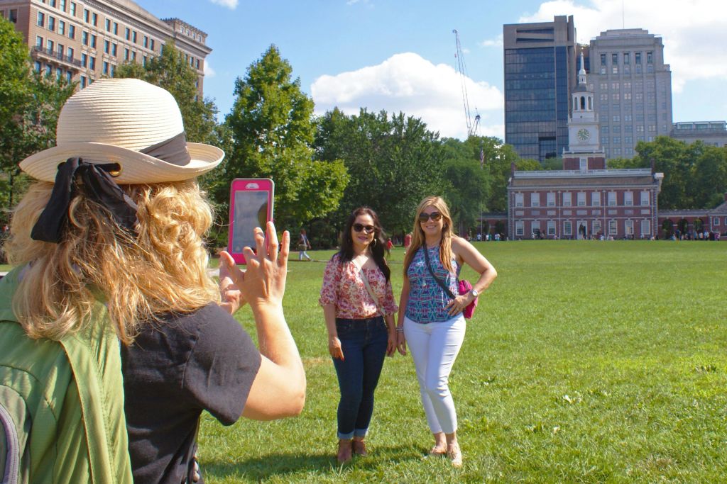 유서 깊은 건물과 고층빌딩을 배경으로 공원에서 두 여성이 포즈를 취하고 있으며, 다른 한 여성이 사진을 찍고 있습니다.