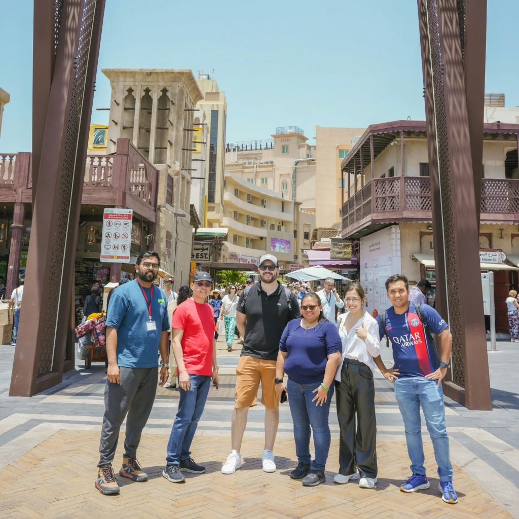 중동의 전통 건축물을 배경으로 상업 지역의 커다란 아치형 통로 아래에 여섯 명이 서 있습니다.