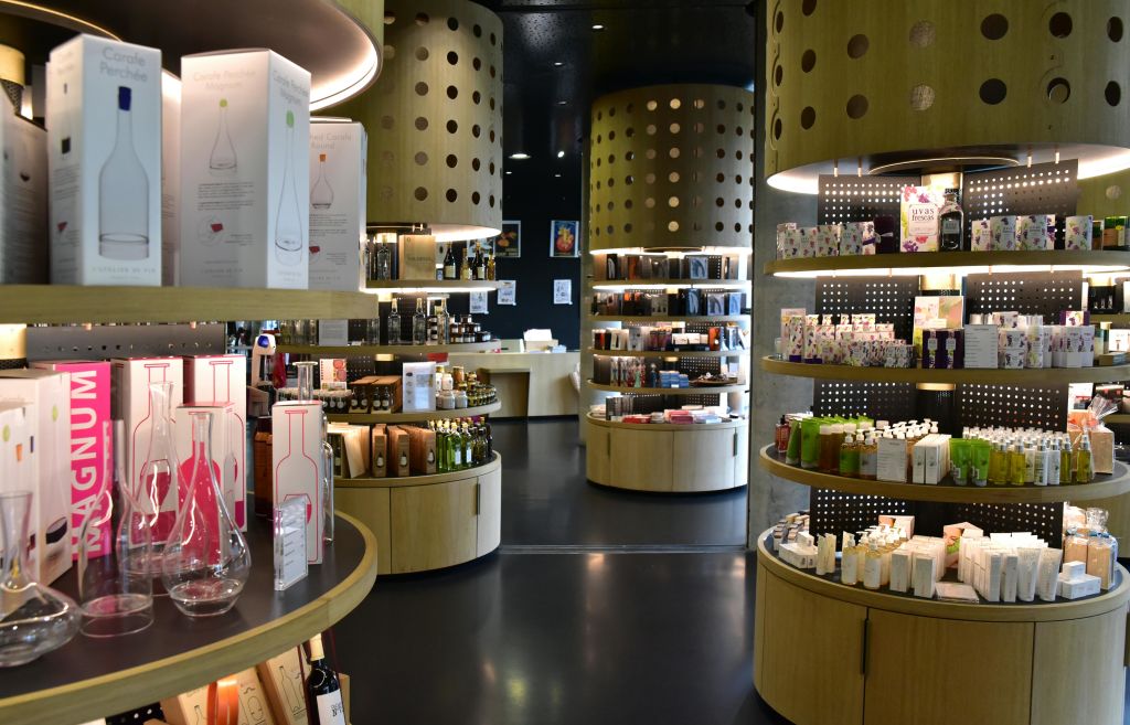 곡선형 목재 선반과 원통형 디스플레이가 있는 현대적인 매장 인테리어로 다양한 병, 상자, 제품을 선보입니다.