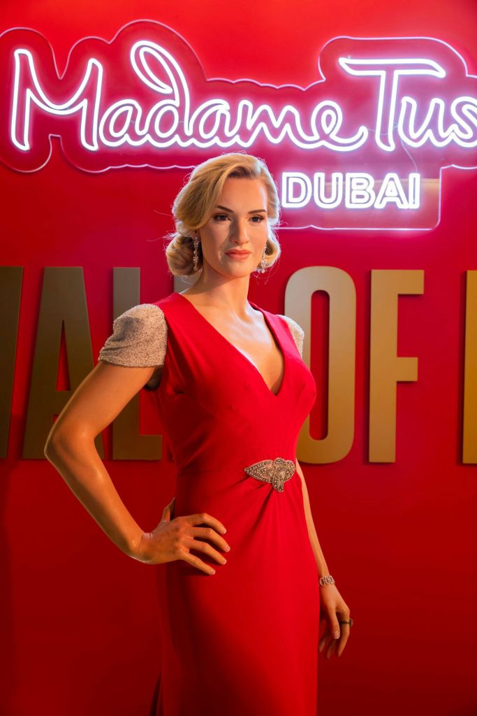 빨간색 드레스를 입은 왁스 피규어와 배경에 네온 사인 "Madame Tussauds Dubai" 가 있습니다.