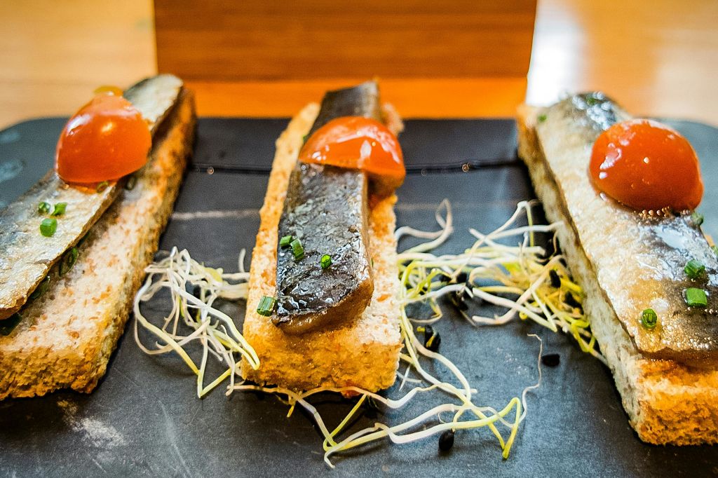 토스트 세 조각에 생선 구이, 체리 토마토 반쪽을 얹고 검은 슬레이트 표면에 나물로 장식했습니다.