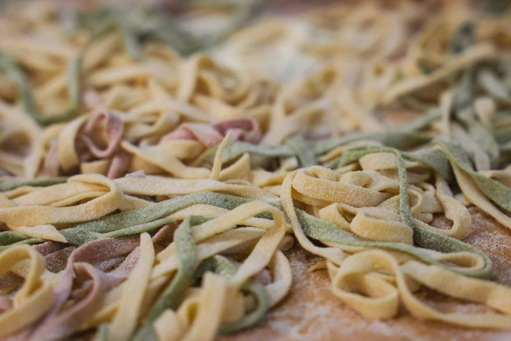 세 가지 색상 (노란색, 녹색, 분홍색) 으로 조리되지 않은 페투치네 파스타를 클로즈업하여 표면에 펴 바릅니다.