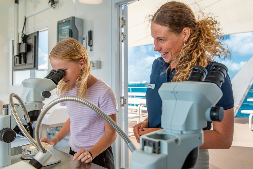 어린이가 현미경을 들여다보고 어른이 옆에 서서 웃고 있습니다. 열린 문으로 야외 경치가 보입니다.