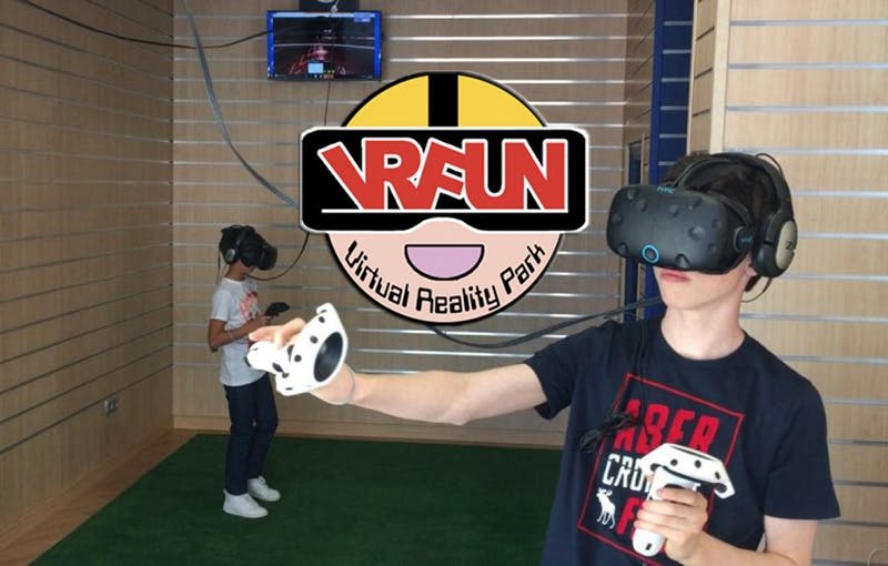 VR 헤드셋을 착용하고 "VRFUN Virtual Reality Park" 로고가 있는 가상 현실 공원에서 컨트롤러를 들고 있는 두 사람.