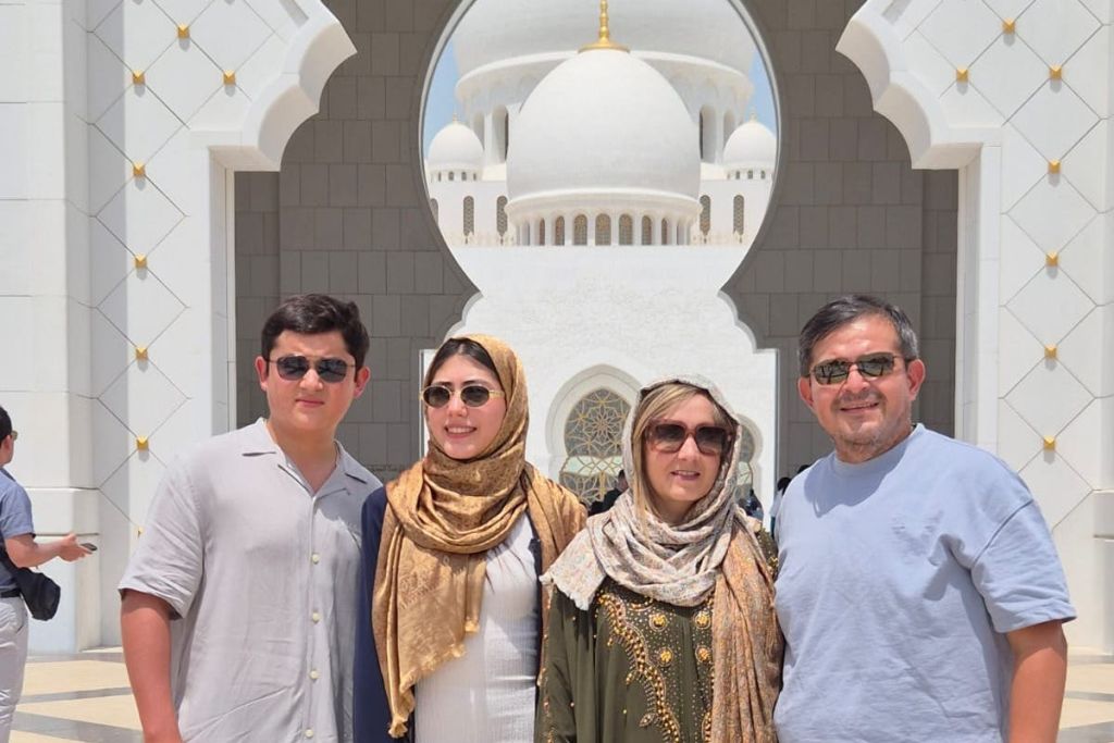 돔형 지붕과 화려한 건축 디테일이 돋보이는 흰색 모스크 앞에서 선글라스를 쓴 세 사람이 포즈를 취하고 있습니다.