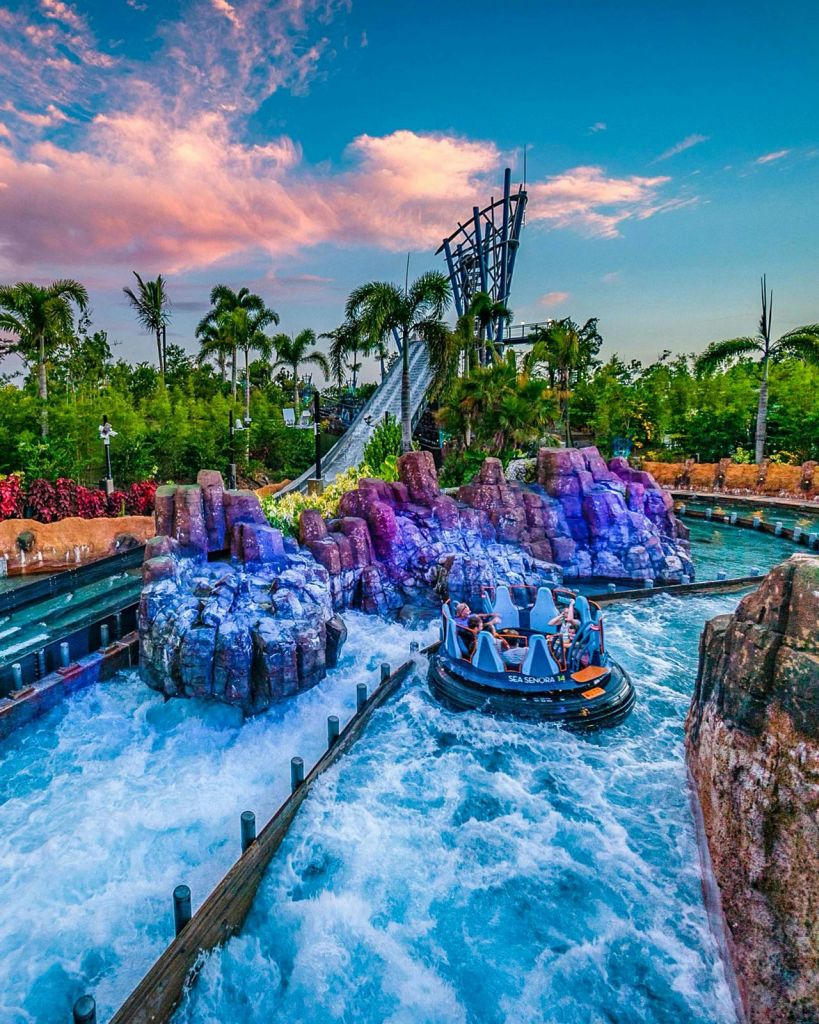 활기찬 일몰 하늘 아래 바위 지형과 녹음이 우거진 수중 코스를 따라 원형 래프팅을 즐기는 사람들.