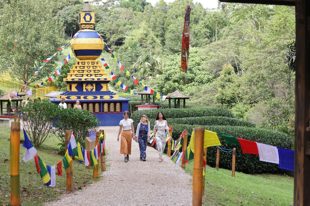 화려한 기도 깃발로 장식된 길을 따라 걷는 세 사람은 울창한 녹색 환경에서 활기찬 스투파로 이어집니다.