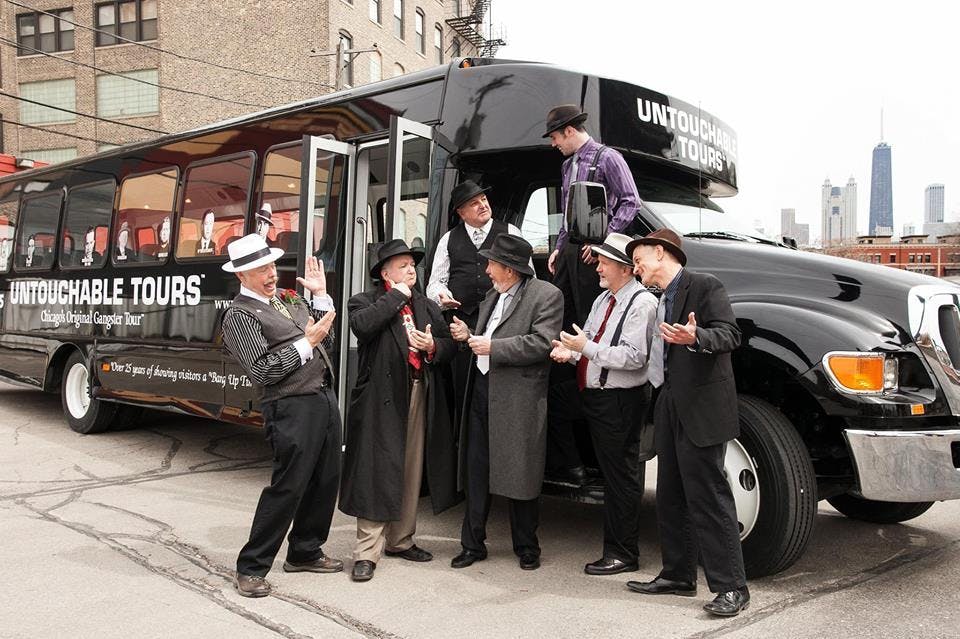 1920년대 스타일의 복장을 한 사람들이 '언터처블 투어 (Untouchable Tours)' 라는 이름의 투어 버스 근처에 서 있습니다.