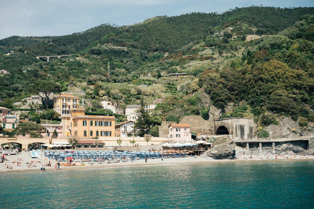 화려한 건물, 해변 파라솔, 일광욕 의자가 있는 해변 마을. 녹음이 우거진 언덕을 배경으로