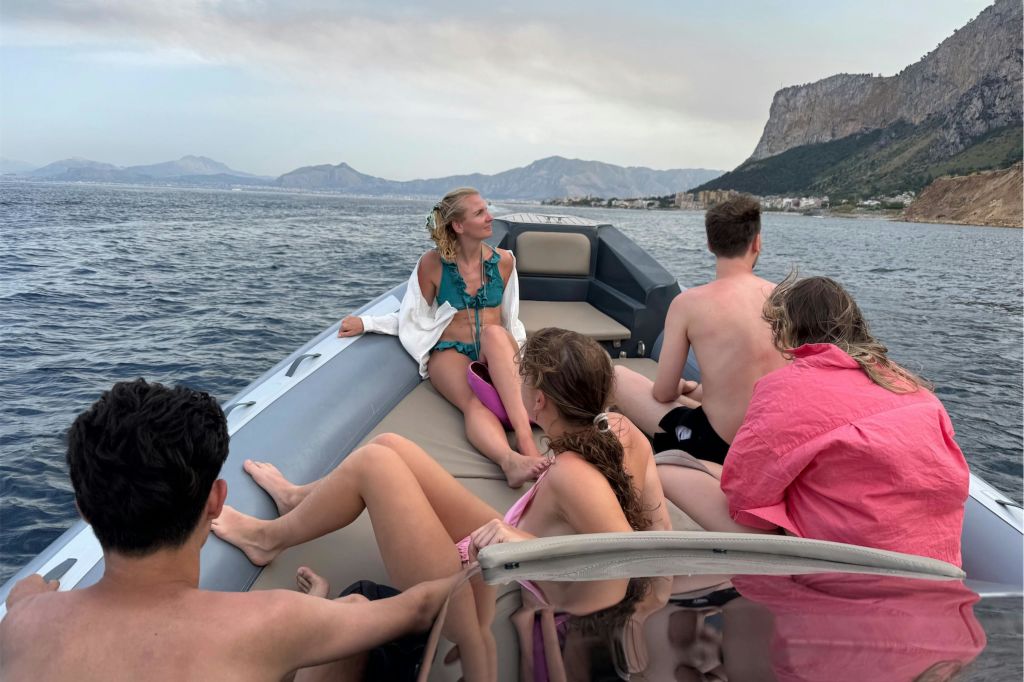 산과 해안선을 배경으로 한 보트에서 수영복을 입은 사람들이 휴식을 취하고 있습니다.