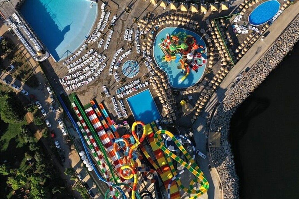 다채로운 미끄럼틀, 수영장, 햇빛 가리개, 라운지 의자가 배치된 워터파크의 공중 전망.