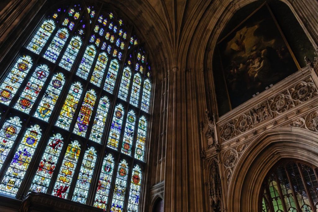벽면의 화려한 석조 건물 옆에 있는 고딕 양식의 건물에 정교한 디자인의 커다란 아치형 스테인드글라스 창문이 있습니다.