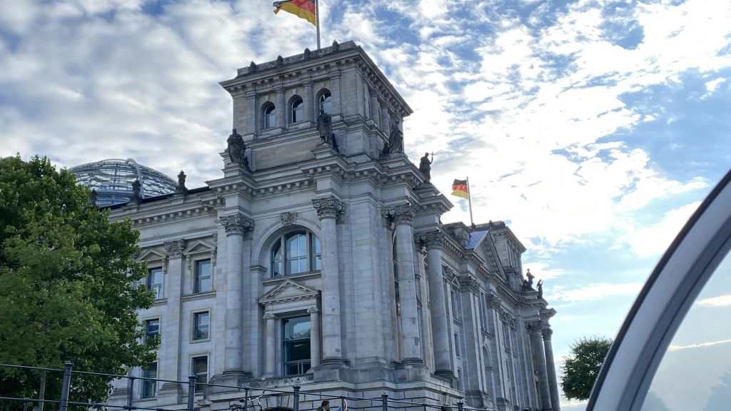 기둥과 화려한 디테일이 돋보이는 역사적인 건물로, 부분적으로 흐린 하늘 아래 상단에 두 개의 깃발이 있습니다.