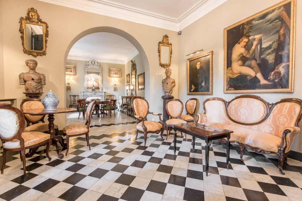 체크무늬 바닥, 앤티크 가구, 액자 그림, 대형 거울, 조각품이 있는 우아한 객실입니다. 아치웨이는 다른 공간으로 이어집니다.