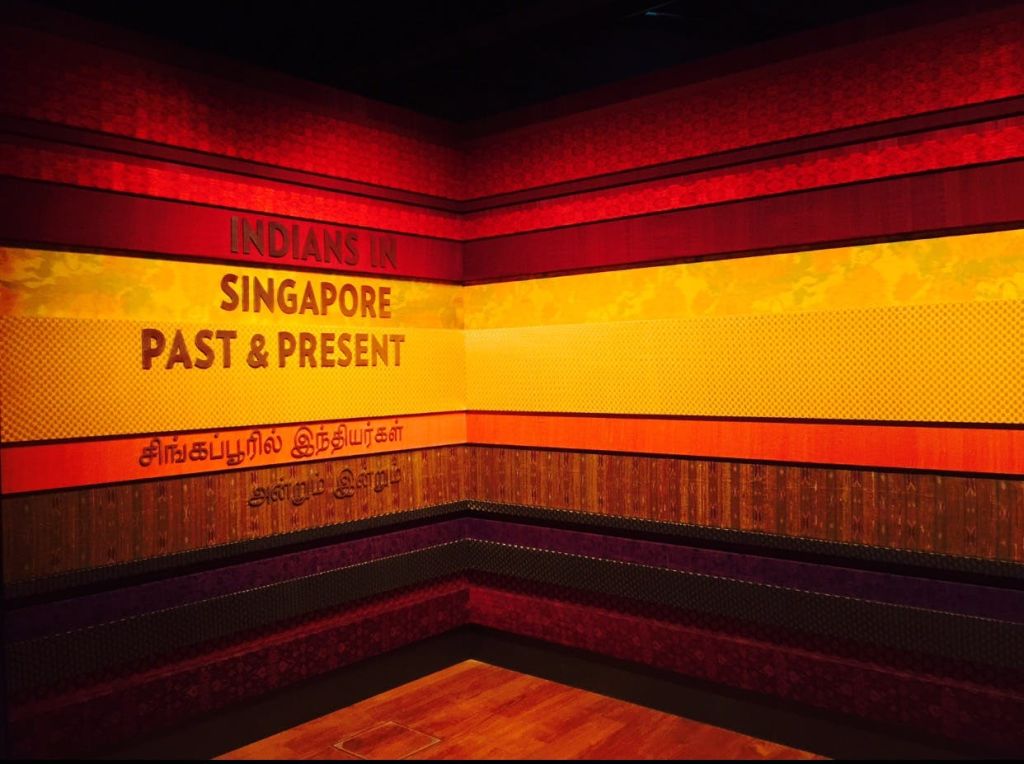 화려한 패턴의 벽과 영어와 타밀어로 된 "Indians in Singapore: Past & Present" 문구가 있는 박물관 전시 코너.