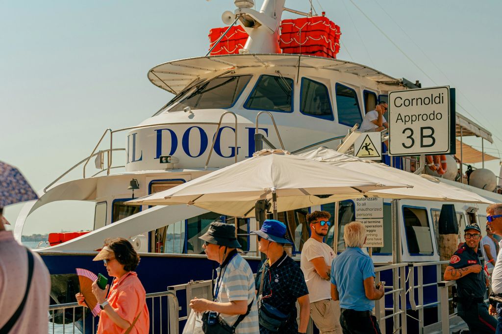 사람들은 "Cornoldi Approdo 3B" 라고 적힌 표지판 아래 도킹된 보트 근처에 서 있습니다.