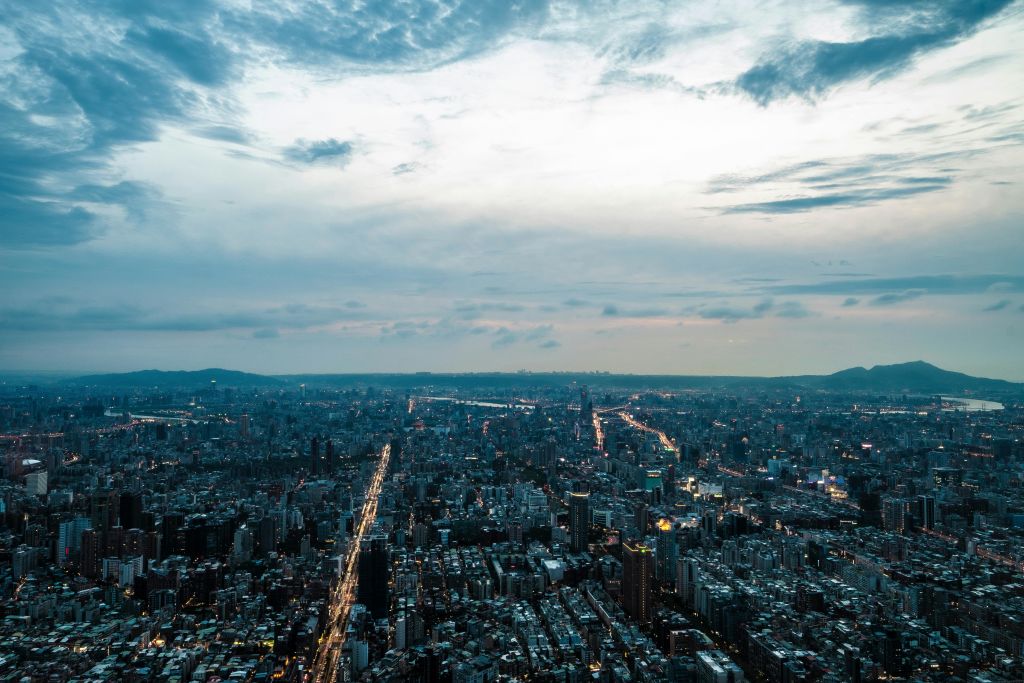 부분적으로 흐린 하늘 아래 건물과 거리가 조명을 받으며 해질 무렵의 도시 풍경을 조망할 수 있습니다.