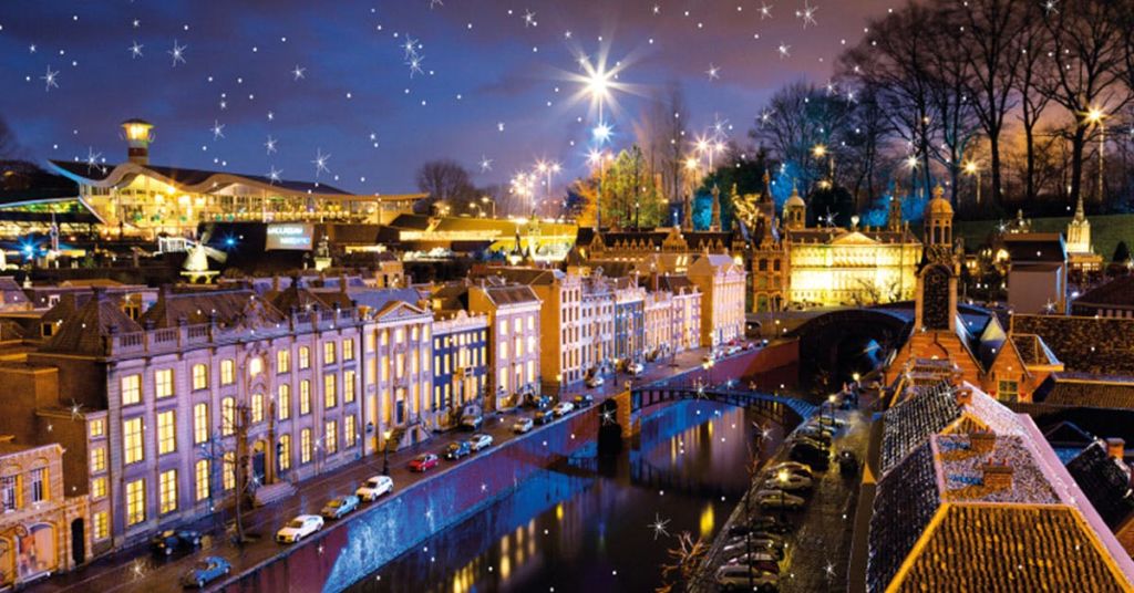 운하를 따라 조명이 켜진 건물, 거리에 주차된 자동차, 별과 같은 장식 조명이 있는 야간 도시 풍경입니다.