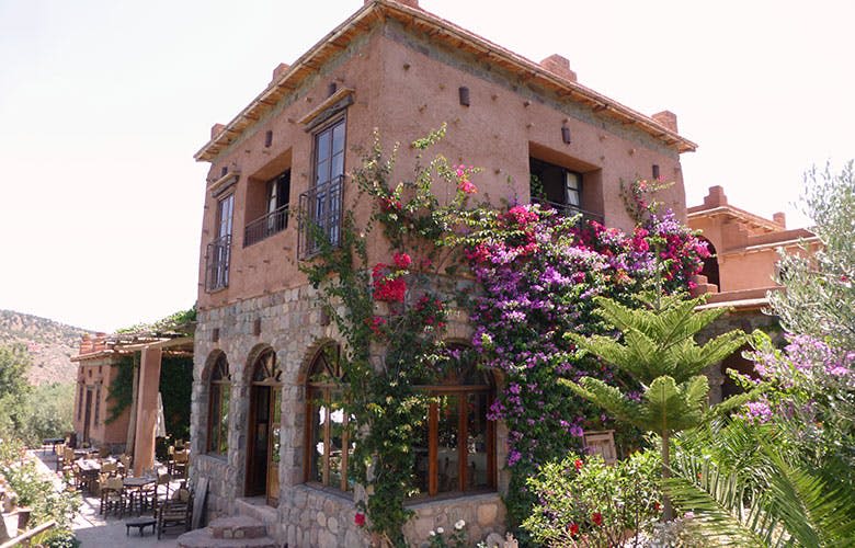 한쪽 면을 덮는 꽃 덩굴, 아치형 창문, 작은 발코니가 있는 2층 소박한 돌과 스투코 하우스.