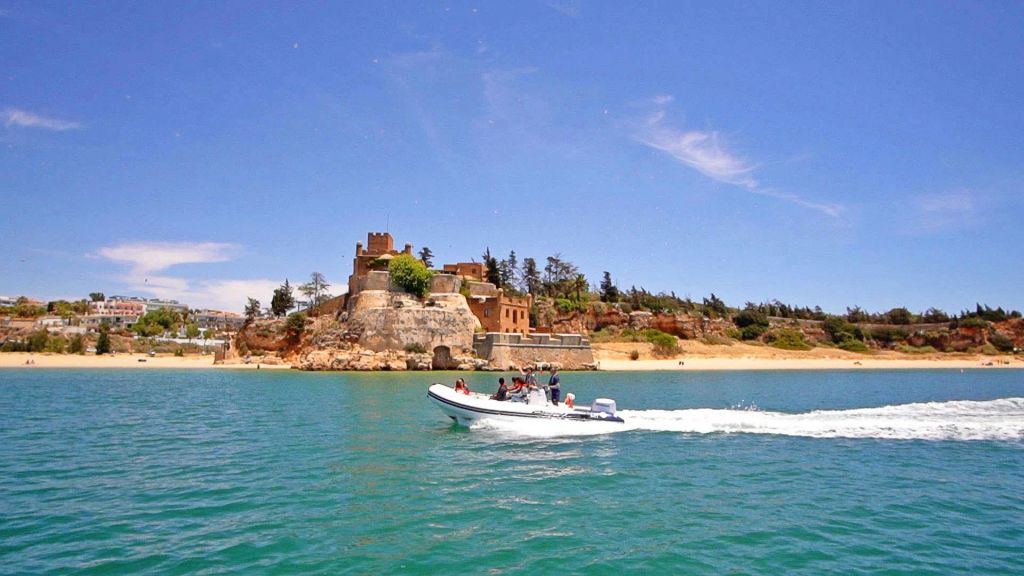 승객이 탑승한 작은 모터보트가 화창한 날 오래된 요새 근처의 푸른 물 위를 여행합니다.