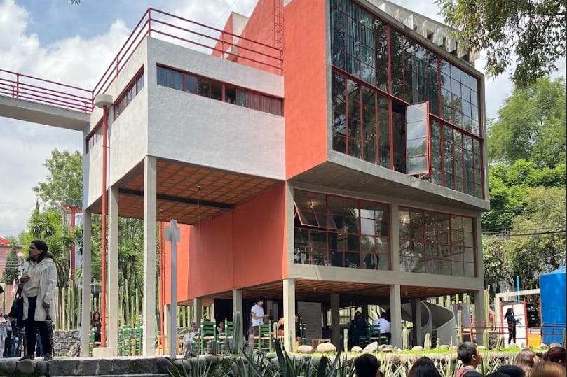 빨간색 주황색 액센트와 커다란 유리창이 있는 현대적인 2층 건물입니다. 사람들은 지상층에 모여 있습니다.