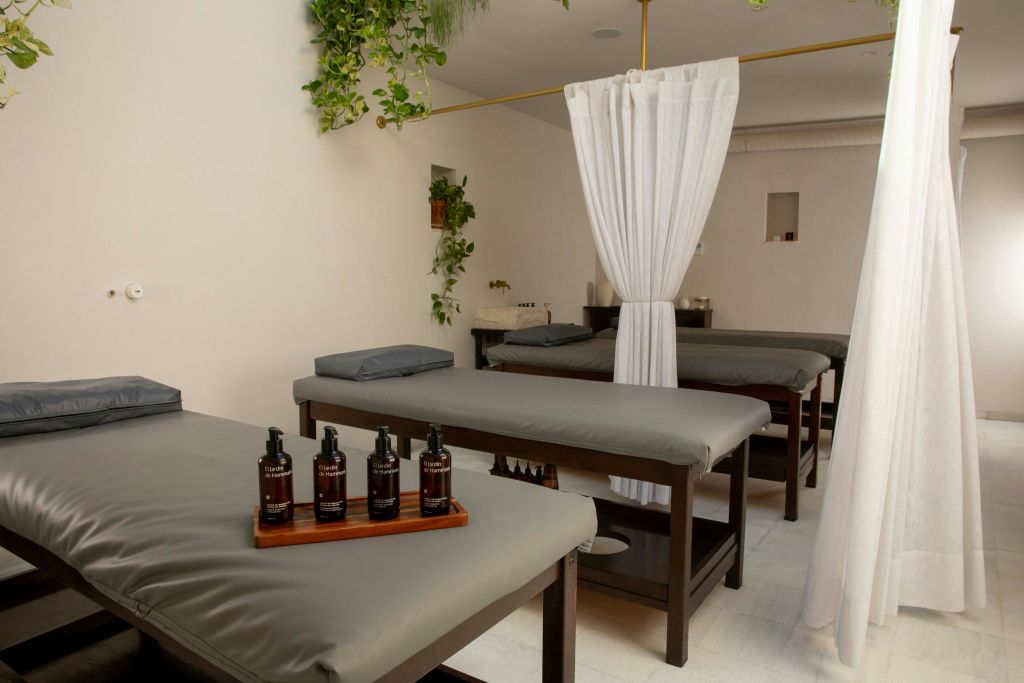 마사지 테이블 여러 개, 스킨케어 제품 트레이, 걸이식물, 프라이버시 커튼이 있는 스파룸입니다.