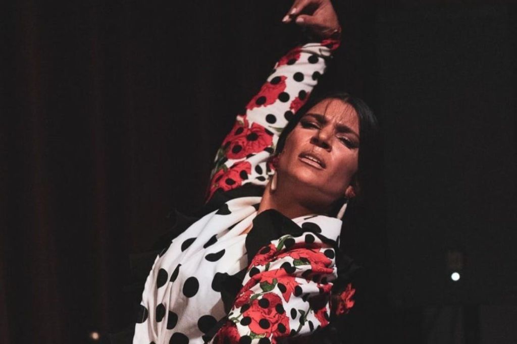 물방울 무늬의 꽃무늬 의상을 입고 춤을 추는 사람. 낮은 조명에서 초점을 맞춘 표정으로 팔을 들어 올립니다.