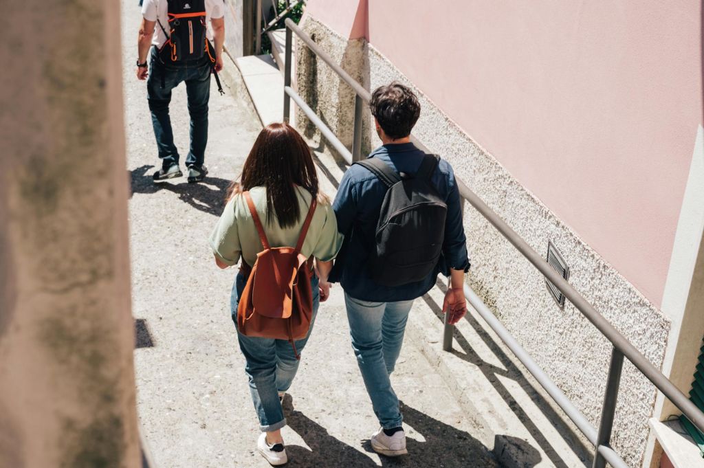 배낭을 메고 난간이 있는 좁은 거리를 걷는 두 사람, 그리고 또 다른 한 사람이 뒤따랐습니다. 오른쪽에 분홍색 벽이 보입니다.