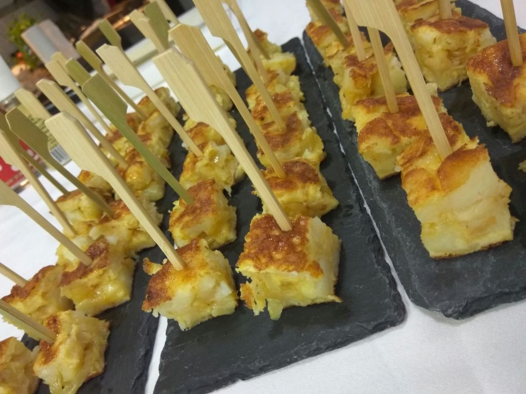 대나무 꼬치가 달린 작은 네모난 스페인 토르티야 조각이 슬레이트 서빙 플래터에 배열되어 있습니다.